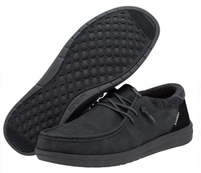 "Pair of Heydude 112294938 men's shoes in all-black color, featuring moc toe stitching, flexible laces, textured knit collar, and a waffle-patterned rubber outsole."