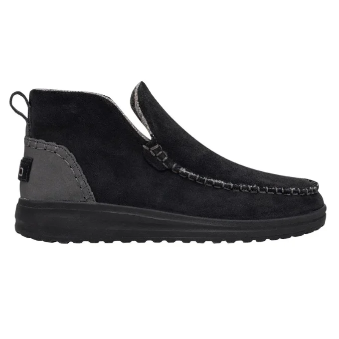"Side view of a black Hey Dude men's shoe, model 122034900, featuring a moccasin-style suede upper, contrast stitching, a pull tab at the heel, and a cushioned black outsole."
