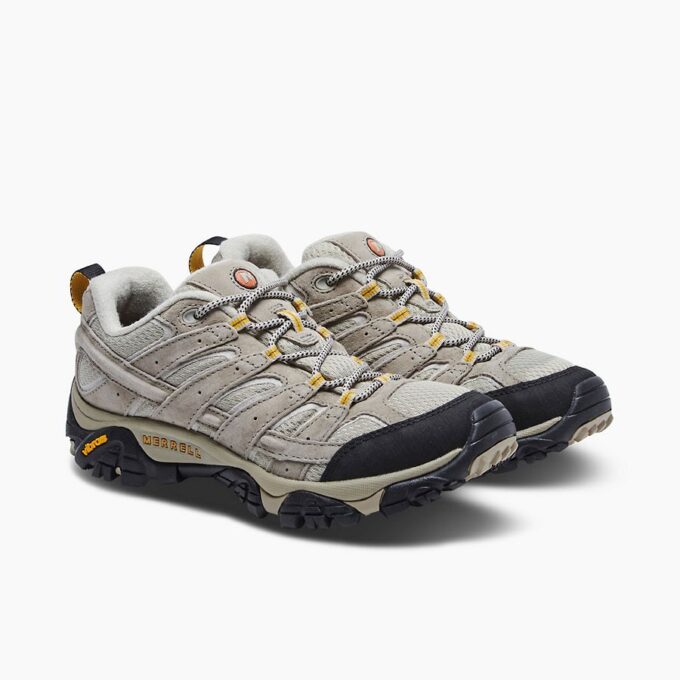 "Pair of beige Merrell J06020 hiking shoes angled to the right, featuring black and white laces with yellow lace loops, black toe caps, padded collars, and Vibram outsoles with the Merrell logo on the side."