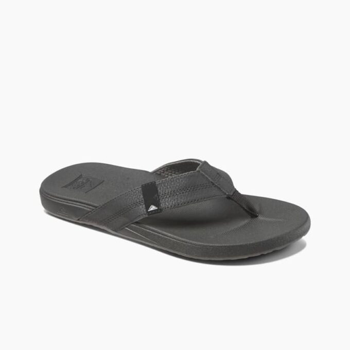 "Angled side view of Reef RF0A3FDIBLA men's black flip-flop sandal with textured footbed, synthetic leather strap, and embossed Reef logo on the heel."