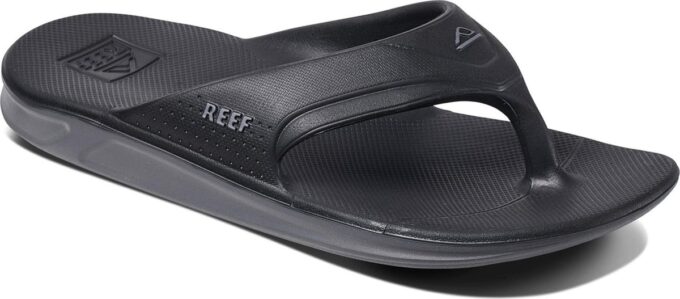 "Angled view of the Reef RF0A3ONCBLA black sandal featuring a contoured footbed, textured sole, and molded thong strap with REEF branding and perforated side detail."