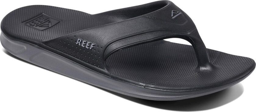 "Angled view of the Reef RF0A3ONCBLA black sandal featuring a contoured footbed, textured sole, and molded thong strap with REEF branding and perforated side detail."