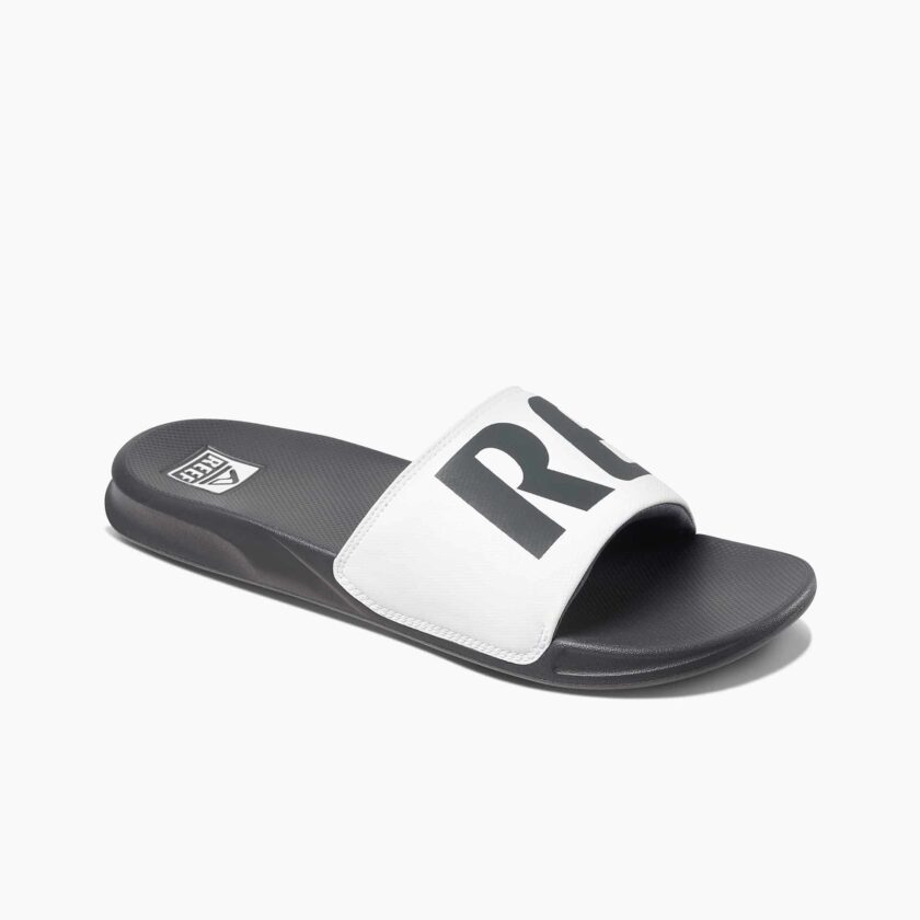 "Angled view of the Reef RF0A3ONDGRW slide sandal featuring a black contoured footbed and a wide white strap with bold black 'REEF' branding."