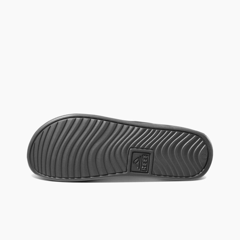 "Bottom view of the Reef RF0A3ONDGRW slide sandal showing a textured black rubber outsole with wavy tread pattern and embossed Reef logo."