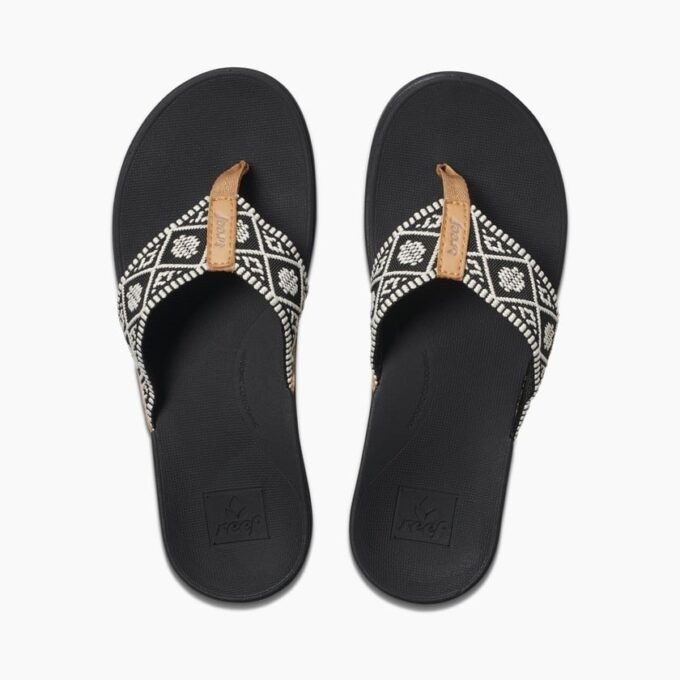 Top view of a pair of Reef RF0A3VDNBLW sandals with black soles and black-and-white patterned fabric straps featuring brown accents and the Reef logo.”