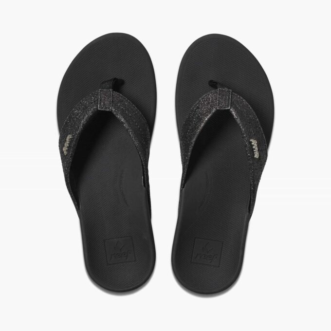 “Top view of black Reef RF0A3VDXBBG flip-flop sandals with glittery fabric straps and cushioned textured footbed featuring the Reef logo.”