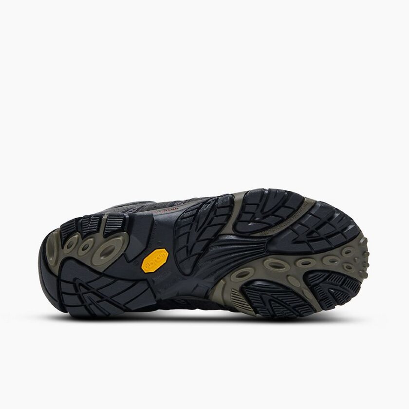 "Close-up of the outsole of a Merrell J06053 hiking shoe in black and olive green, featuring a rugged tread pattern and a yellow Vibram logo on the sole against a white background."