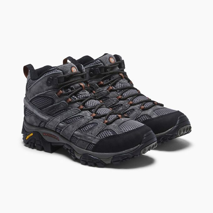 "Pair of Merrell J06053 hiking shoes in dark gray with black and orange accents, shown from a front-side angle on a white background. The shoes feature mesh and suede uppers, black toe caps, black and orange laces, and Vibram soles."