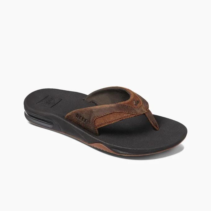 “Angled view of a Reef RF002156BRZ sandal featuring brown suede straps, black textured footbed, and a visible air-cushion sole for enhanced comfort.”