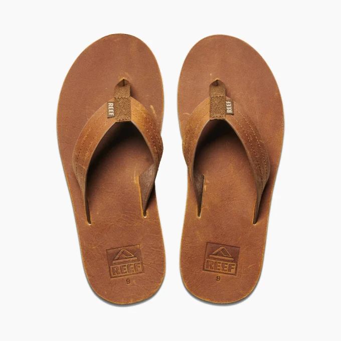 "Top view of a pair of tan leather Reef flip-flops with stitched straps and embossed logos on the footbeds."