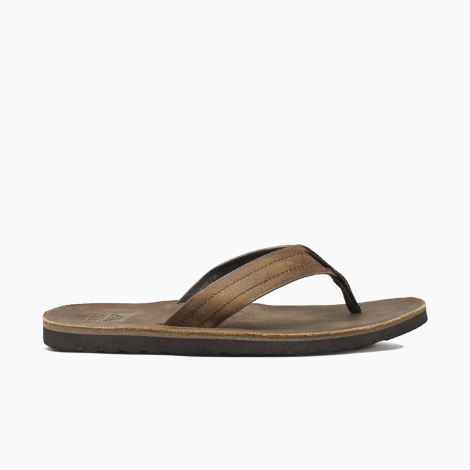 "Side view of brown Reef RF0A2YFRDAB flip-flop with thick strap and dark sole, showing textured footbed and stitching detail."