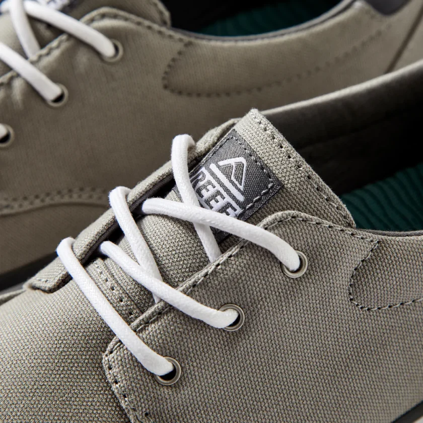 "Close-up view of Reef RF0A3FE4GRW casual shoe in gray, showcasing the white laces, textured canvas upper, and woven Reef logo tag on the tongue."