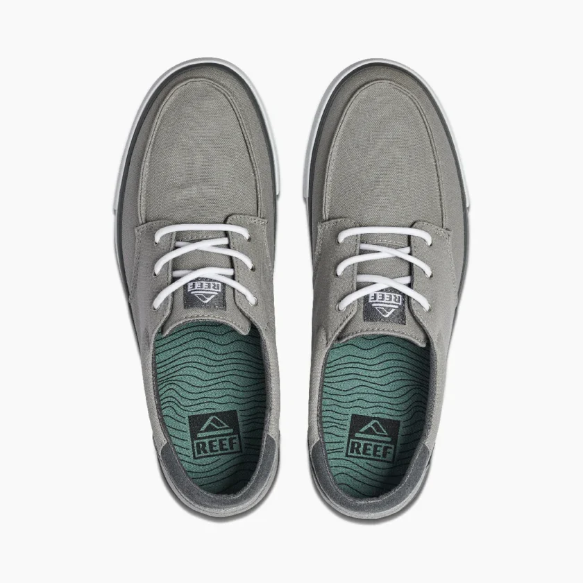 "Top view of a pair of gray Reef RF0A3FE4GRW casual shoes featuring white laces, green insoles with wave pattern, and black Reef branding on the heel and tongue."