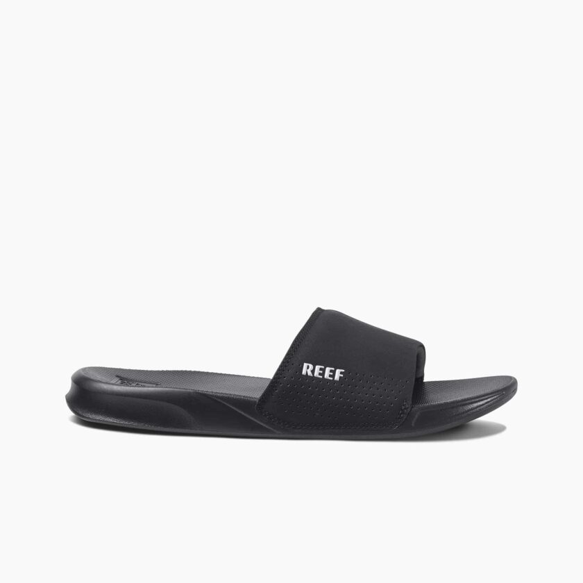 "Side view of a black Reef RF0A3ONDBLA slide sandal featuring a perforated strap with the white Reef logo and a contoured footbed."