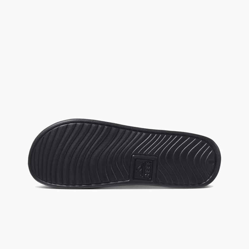 "Bottom sole view of a black Reef RF0A3ONDBLA slide sandal showing the wavy tread pattern and embossed Reef logo in the center."