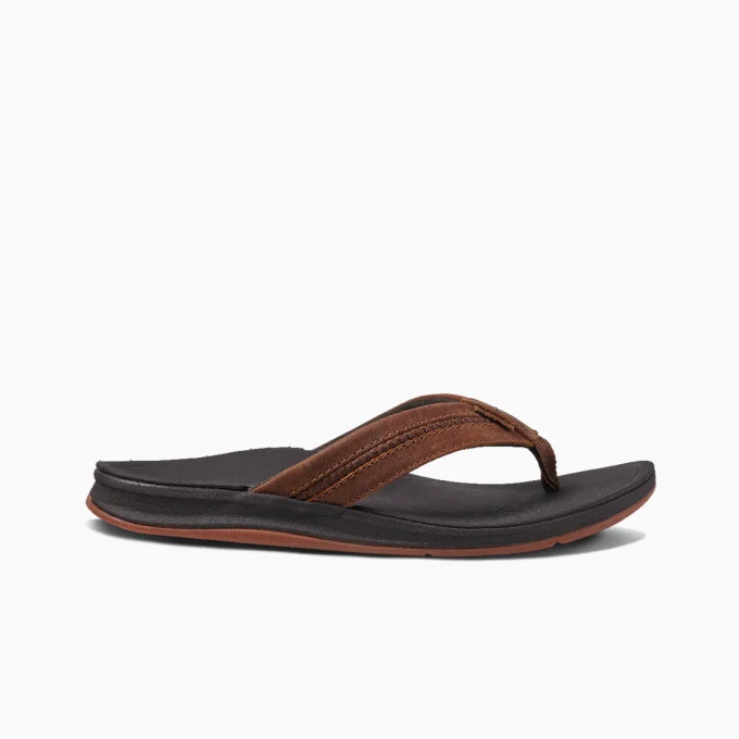 "Side profile of a brown leather Reef flip-flop with a dark cushioned footbed and a brown rubber outsole."