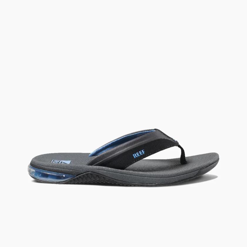 "Side view of a Reef RF0A3YMIGBL sandals featuring black straps with blue lining, textured dark gray footbeds, and blue Reef logos printed near the heel area."