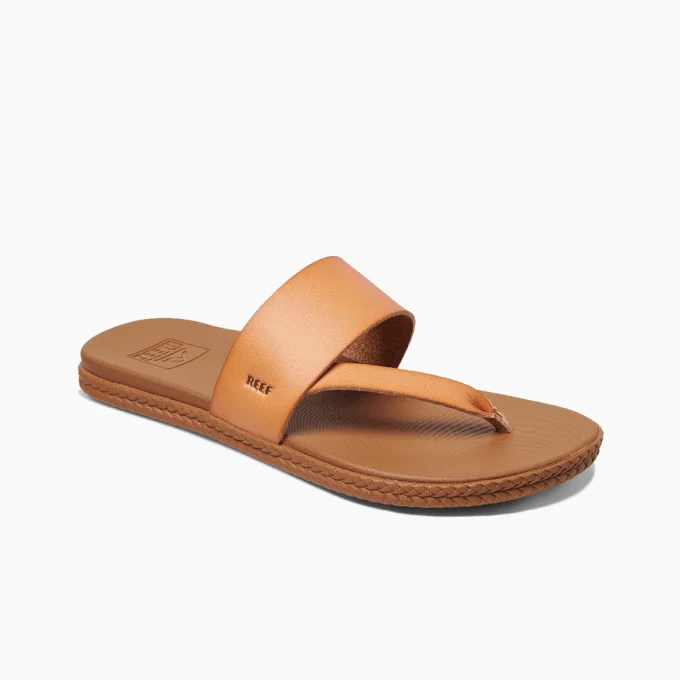 “Side view of a tan Reef RF0A3YNFNAT sandal with a wide leather strap and toe thong, featuring the Reef logo embossed on the strap and a braided textured sole edge.”