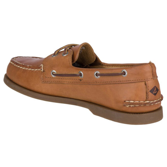 "Angled rear-side view of a tan Sperry A/O Sahara boat shoe featuring rawhide laces threaded through metal eyelets, moc-toe stitching, and a brown rubber outsole with Sperry’s sailboat logo on the heel."