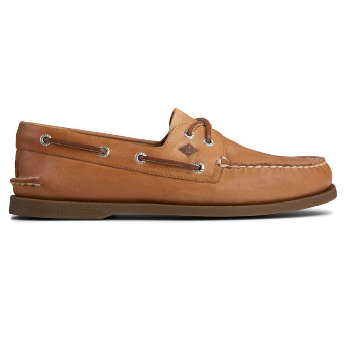 "Side view of a tan Sperry A/O Sahara boat shoe featuring rawhide laces threaded through metal eyelets, moc-toe stitching, and a brown rubber outsole with Sperry’s sailboat logo on the heel."